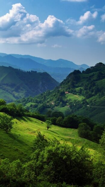 A scenic view of Cantabrian Mountains with lush green hills and a partly cloudy sky