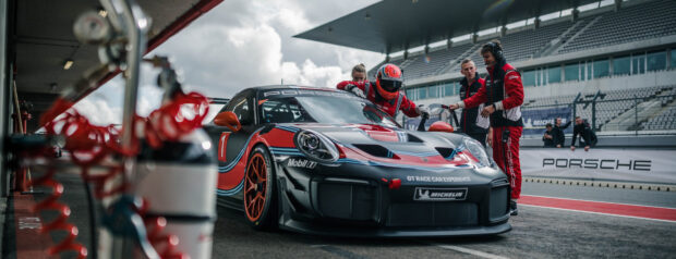 A race car driver preparing to enter the racing car in the pit with a team assisting