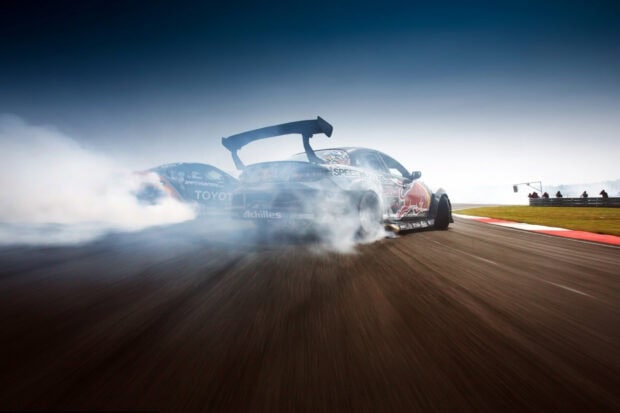 Two race cars drifting and creating smoke on the track during a car race
