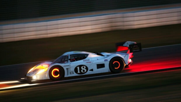 A race car speeding on the track with glowing wheels and bright headlights at night