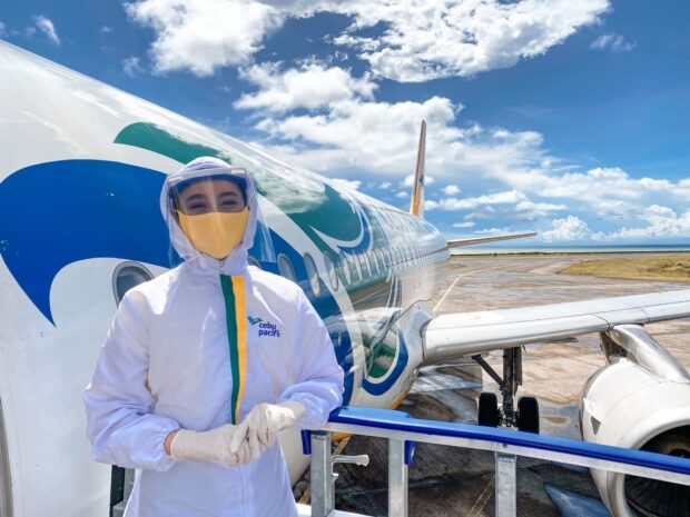 A Cebu Pacific Air crew member stands beside the plane wearing safety gear and a mask on the runway, HD Desktop Wallpaper