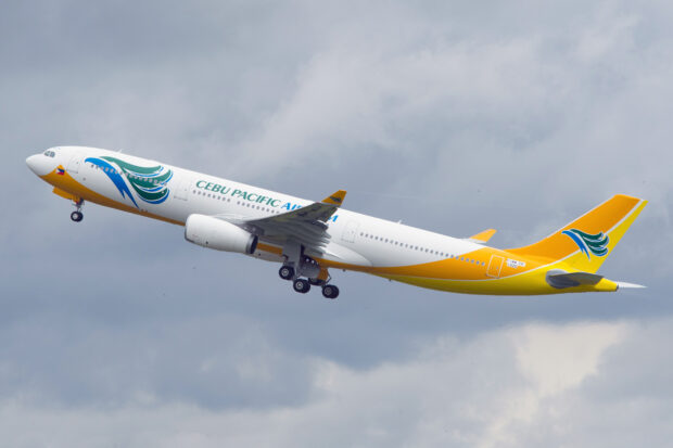 A Cebu Pacific Air airplane is captured flying through a cloudy sky with its landing gear partially retracted, HD Desktop Wallpaper