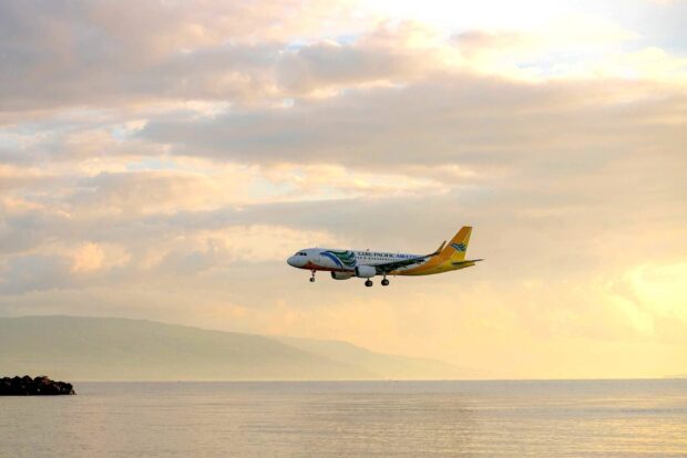 A Cebu Pacific Air plane is flying low over the water near a mountainous coastline, HD Desktop Wallpaper