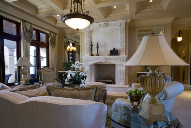 A chandelier hanging from a detailed ceiling in a luxurious living room with elegant furniture and decor