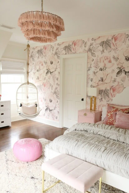 Pink tassel chandelier hanging in a bedroom with floral wallpaper and soft furnishings