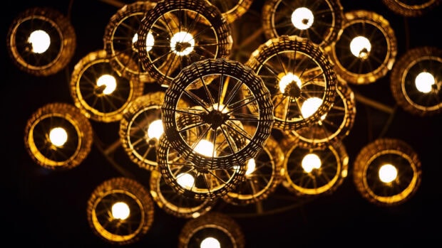 Warm glowing chandelier design with intricate circular woven frames illuminating dark background