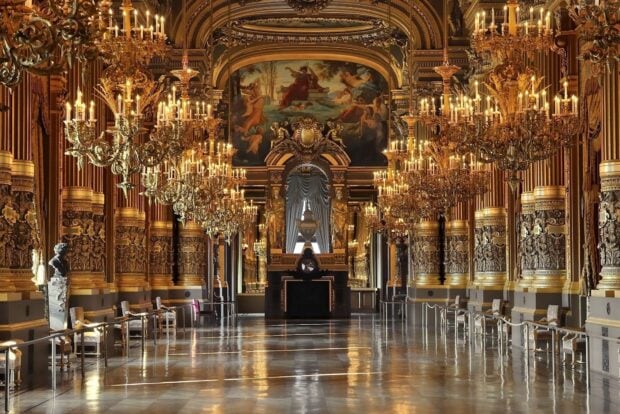 Ornate chandelier lighting in a grand hall with detailed golden architecture and reflective floor