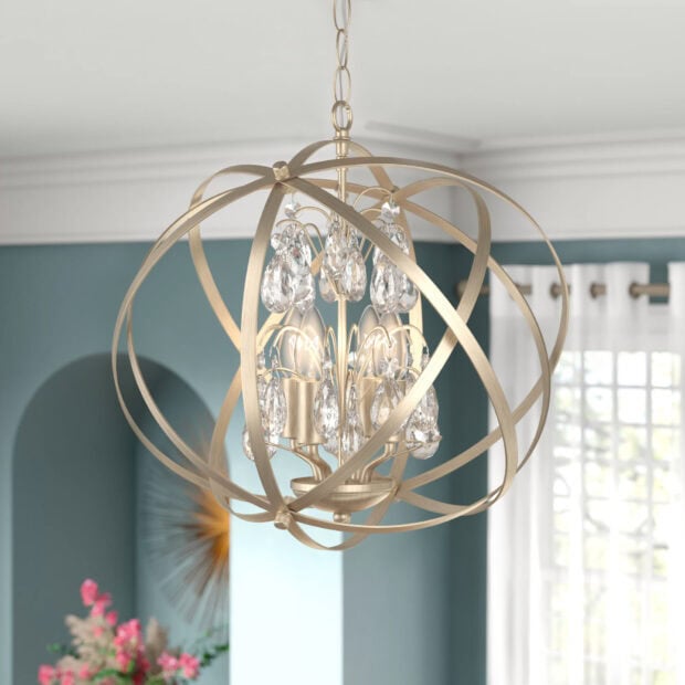 A modern chandelier with crystal drops inside a spherical metal frame hanging in a living room
