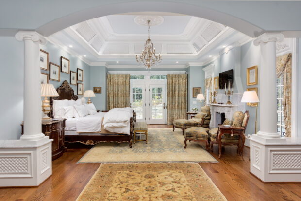 A chandelier hanging from the ceiling in a spacious bedroom with classic furniture and elegant decor