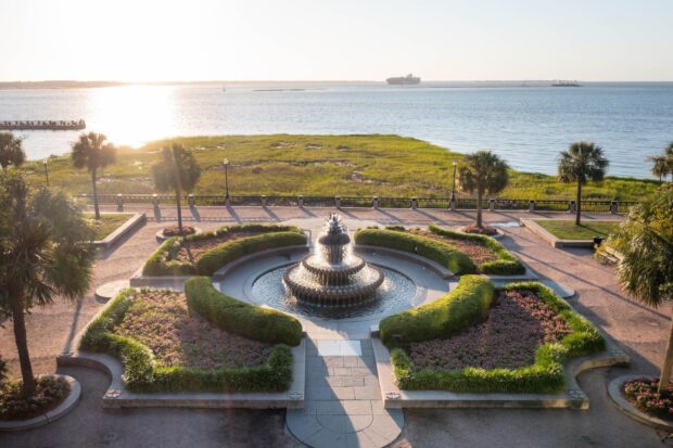 A scenic view of Charleston South Carolina featuring the Pineapple Fountain and waterfront park at sunset