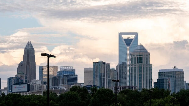 The Charlotte North Carolina skyline is seen under a cloudy sky with tall buildings and green trees, HD Desktop Wallpaper