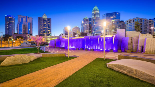The Charlotte North Carolina skyline glows with illuminated buildings and a purple lit fountain in the park, HD Desktop Wallpaper