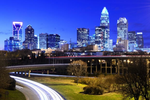 The Charlotte North Carolina skyline features illuminated skyscrapers and light trails from vehicles on busy roads, 2K Desktop Wallpaper
