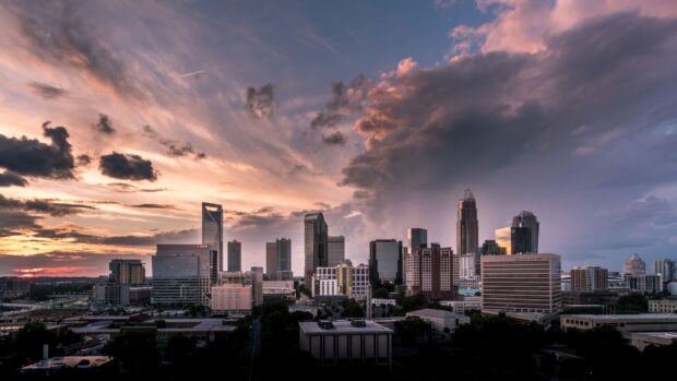 The Charlotte North Carolina skyline is seen under a dramatic sunset sky with clouds and sunlight, 2K Desktop Wallpaper