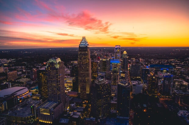 A vibrant view of Charlotte North Carolina skyline during sunset with illuminated buildings, 2K Desktop Wallpaper