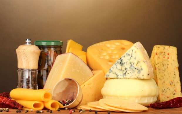 A variety of cheese pieces with peppercorns and dried chili peppers arranged on a wooden surface