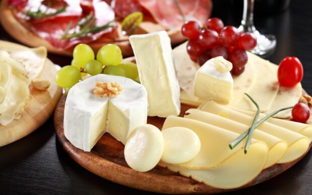Assorted cheese varieties on a wooden platter with grapes and herbs