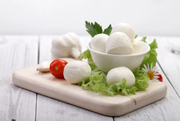 Fresh cheese balls arranged on lettuce with cherry tomato and garlic on wooden board