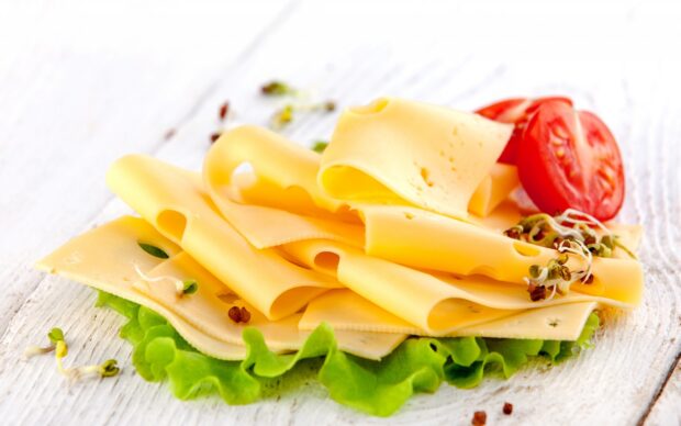 Slices of cheese arranged on lettuce with tomatoes and sprouts on a wooden surface