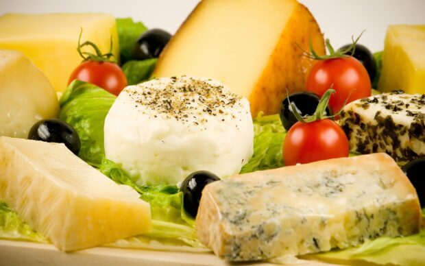 A delicious assortment of cheese on fresh lettuce with cherry tomatoes and black olives sprinkled with herbs