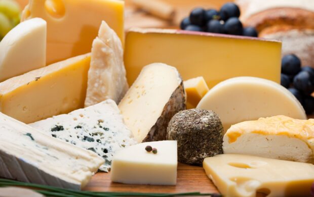 A selection of various cheese types arranged on a wooden board with grapes in the background