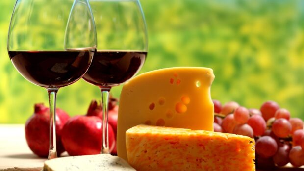 A cheese assortment with red wine glasses and fresh fruits on a table