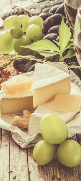 A close up of cheese with green grapes and nuts on wooden surface