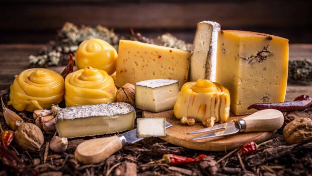 Various types of cheese arranged on a rustic wooden board with nuts and spices surrounding the cheese