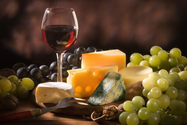 A selection of cheese varieties with grapes and a glass of red wine on a wooden board