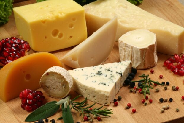 A variety of cheese including blue cheese and gouda on a wooden board with herbs and pomegranate seeds
