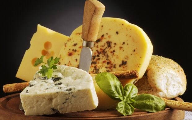 A variety of cheese with herbs and a knife on a wooden board