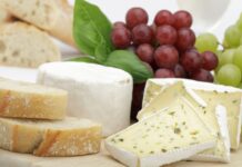 Soft cheese with herbs and fresh bread slices displayed with grapes and basil leaves