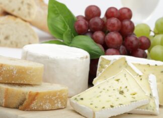Soft cheese with herbs and fresh bread slices displayed with grapes and basil leaves