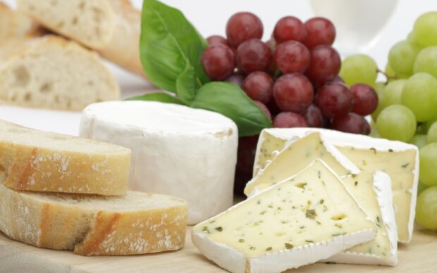 Soft cheese with herbs and fresh bread slices displayed with grapes and basil leaves