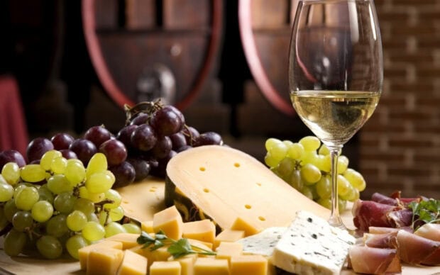 A platter of cheese with grapes and a glass of white wine in a rustic setting