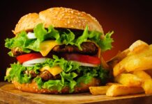 Juicy cheeseburger with lettuce, tomato, onion, and crispy fries on a wooden surface.