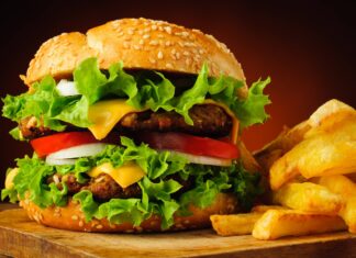 Juicy cheeseburger with lettuce, tomato, onion, and crispy fries on a wooden surface.