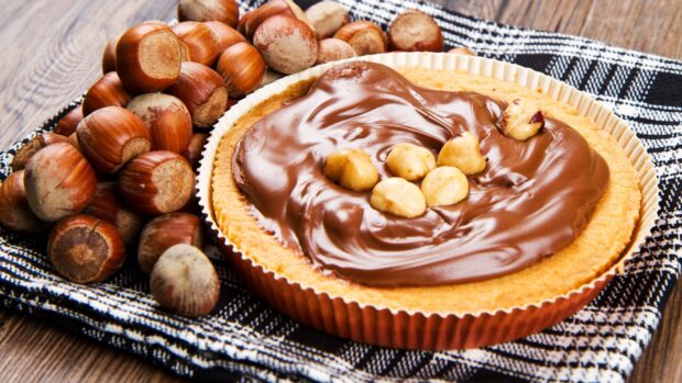 A delicious pie topped with chocolate hazelnut spread and whole hazelnuts is placed on a checkered cloth, 4K Desktop Wallpaper
