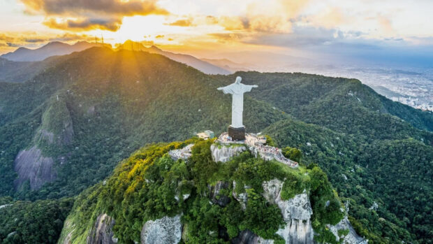 The Christ The Redeemer statue stands tall over lush green hills during a golden sunset, HD Desktop Wallpaper