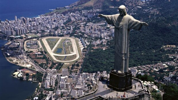 The Christ The Redeemer statue overlooks the cityscape of Rio de Janeiro with lush greenery and urban buildings, HD Desktop Wallpaper