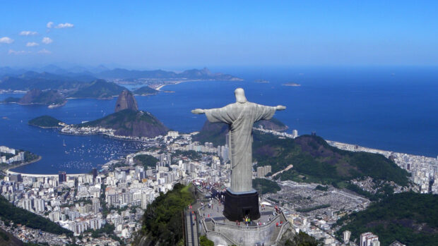 The Christ The Redeemer statue stands tall above the city of Rio de Janeiro with mountains and ocean in the background, 4K Desktop Wallpaper