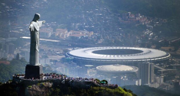 The Christ The Redeemer statue stands tall above the city with a stadium in the background, 2K Desktop Wallpaper