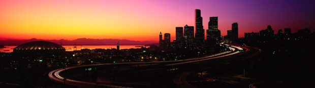 The city skylines with lit buildings and curved highway under a vibrant sunset sky