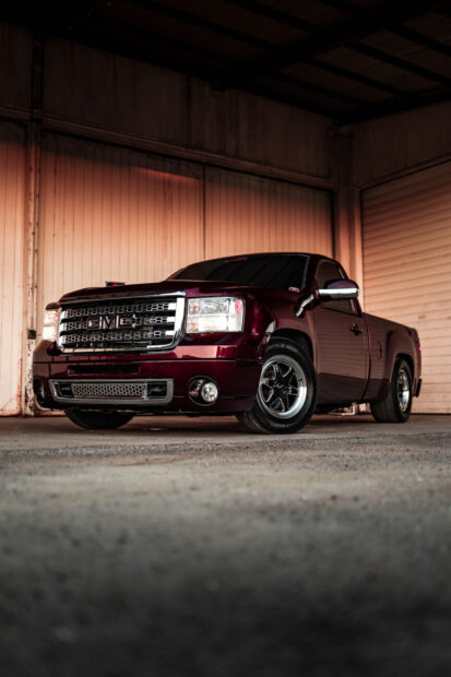 A maroon GMC truck is parked inside a spacious industrial garage with soft lighting, HD Mobile Wallpaper