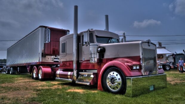 A classic Kenworth truck is parked on grass with a trailer attached and cloudy sky above, 2K Desktop Wallpaper