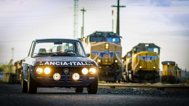 A vintage Lancia car is parked near railway tracks with trains behind it, HD Desktop Wallpaper