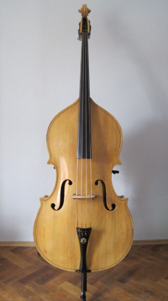 A classic double bass is shown standing on a wooden floor against a plain wall in this double bass wallpapers, 2K Desktop Wallpaper