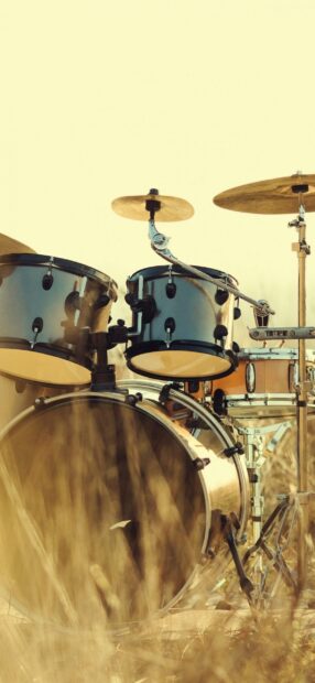 A classic drum set stands among tall grass in a sunny field with warm tones, 2K Phone Wallpaper