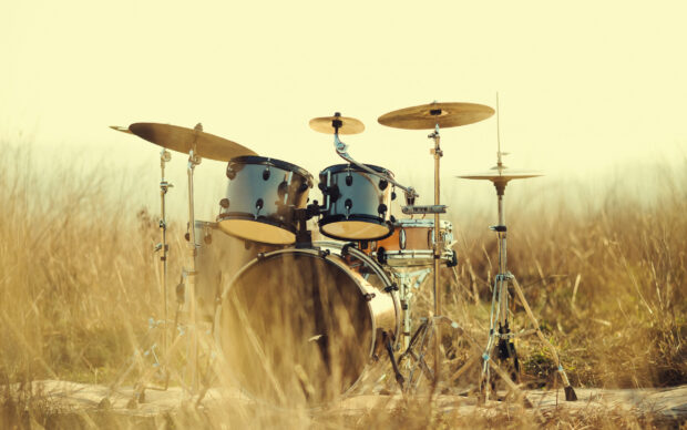 A classic drum set stands alone in a dry grassy field under warm sunset light, 2K Desktop Wallpaper