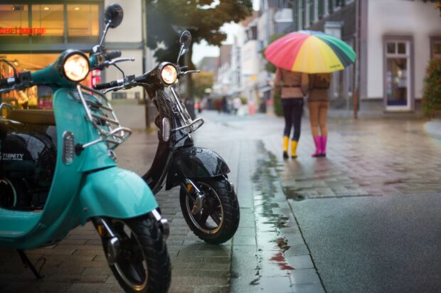 Two scooters stand on a wet street while two people walk under a colorful umbrella, HD Desktop Wallpaper